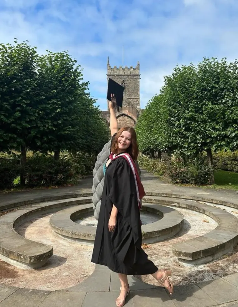 Graduate raising her cap in the university gardens